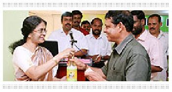 Mrs. Mini Mathew Giving the first bottle of Virgin Plus to Sri Rajendran, Chairman, Horticorp